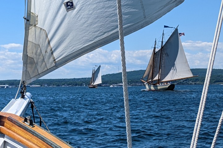 Sailboats on a lake with mountains in the background, seen from another boat.