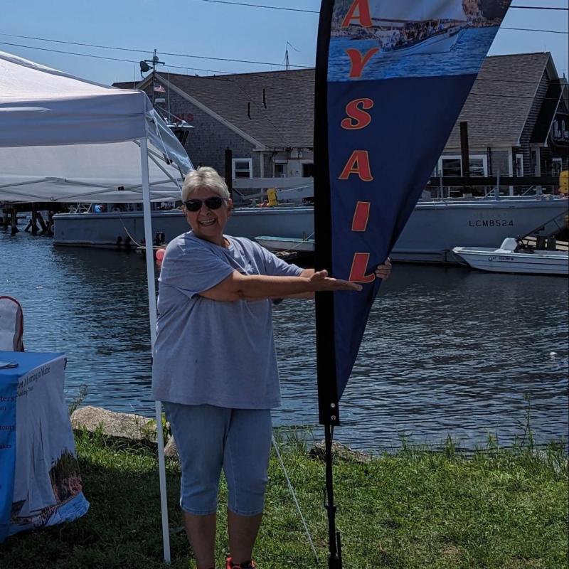 Woman pointing to 'Day Sails' flag by waterfront tent.