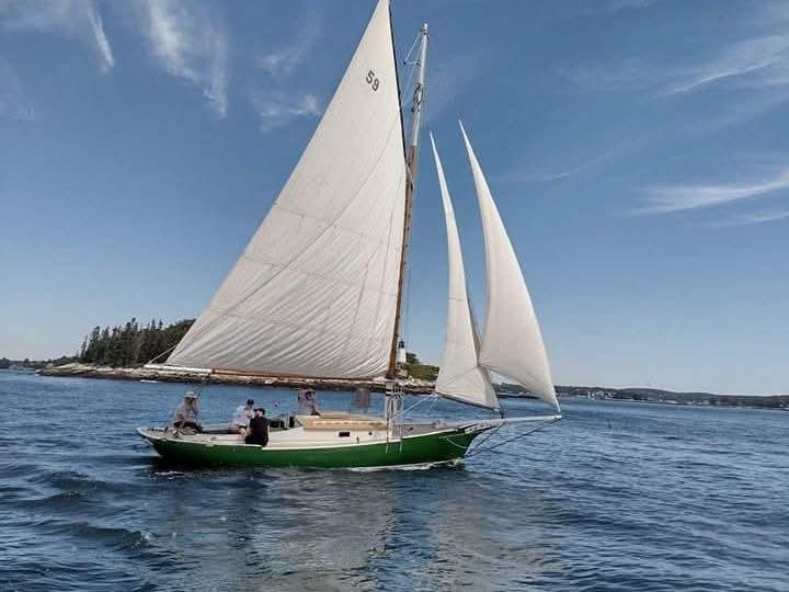 Green sailboat with white sails on a calm sea under a blue sky.
